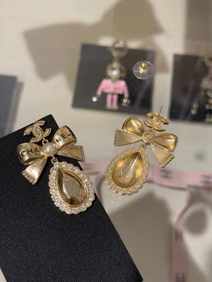 Boucles d'oreilles pendantes en cristal en forme de goutte d'eau avec lettres sculptées double C, perles et nœud doré.