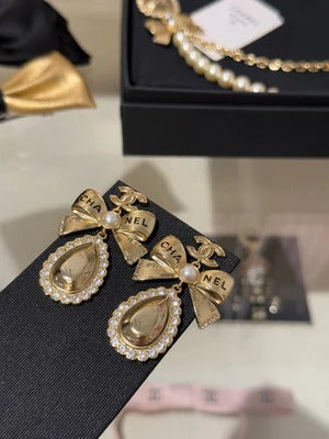 Boucles d'oreilles pendantes en cristal en forme de goutte d'eau avec lettres sculptées double C, perles et nœud doré.