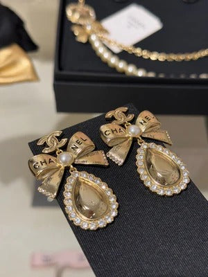 Boucles d'oreilles pendantes en cristal en forme de goutte d'eau avec lettres sculptées double C, perles et nœud doré.