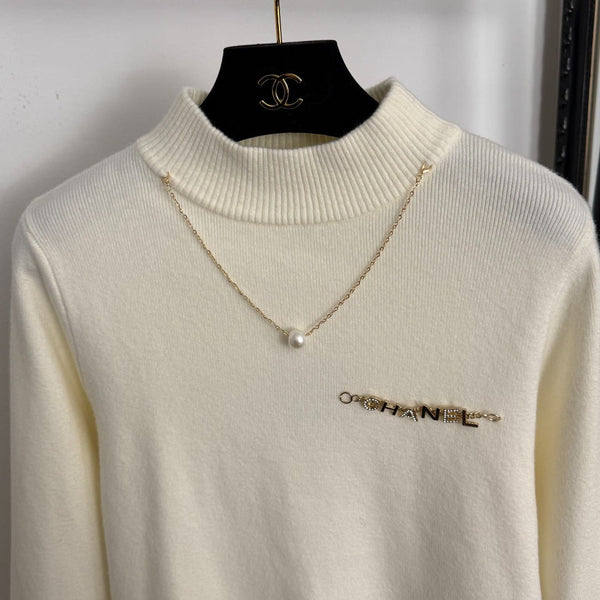 Top en maille à manches longues avec pompon et collier doré en métal siglé Chanel