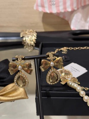 Boucles d'oreilles pendantes en cristal en forme de goutte d'eau avec lettres sculptées double C, perles et nœud doré.