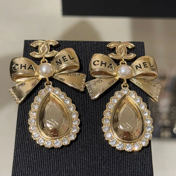 Boucles d'oreilles pendantes en cristal en forme de goutte d'eau avec lettres sculptées double C, perles et nœud doré.